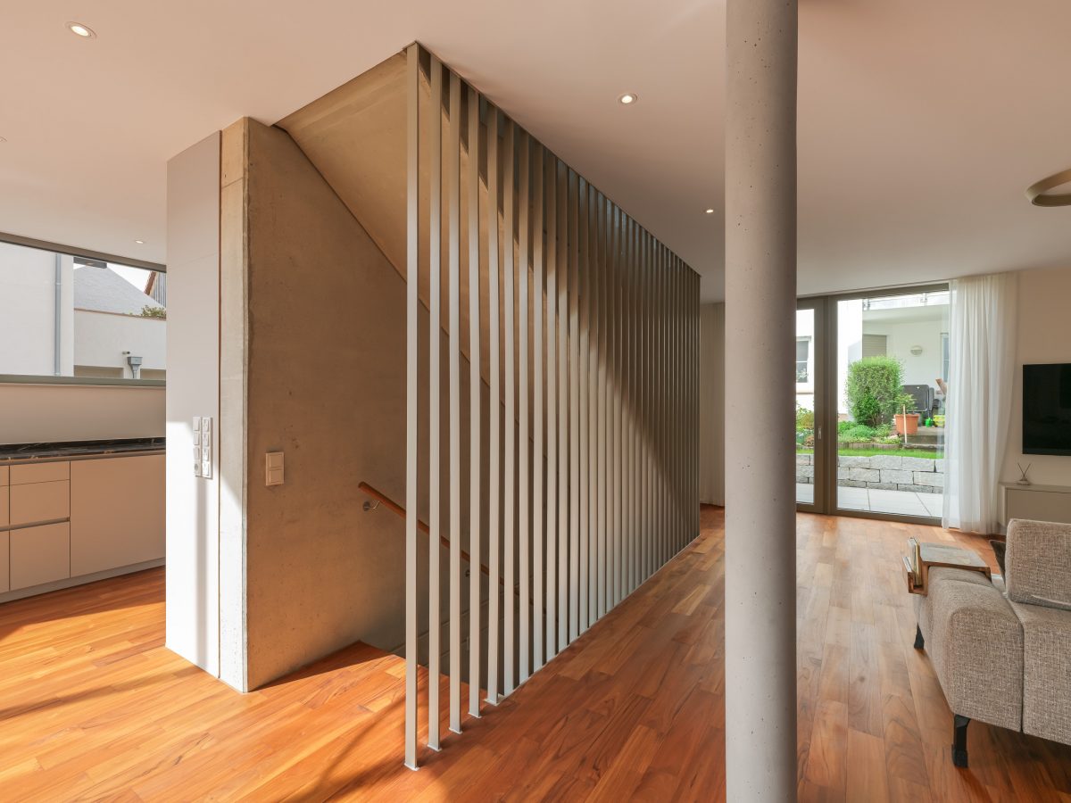 Zentraler Treppenaufgang entlang einer dreigeschossigen Sichtbetonwand als vertikales Erschließungselement im kompakten Einfamilienhaus.
