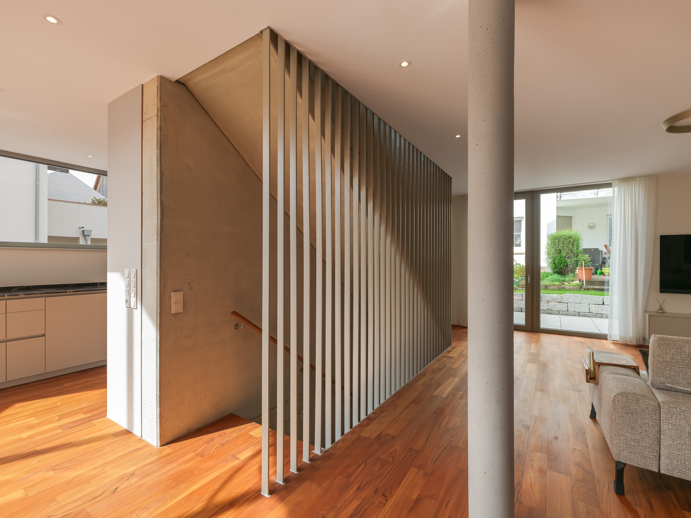 Zentraler Treppenaufgang entlang einer dreigeschossigen Sichtbetonwand als vertikales Erschließungselement im kompakten Einfamilienhaus.