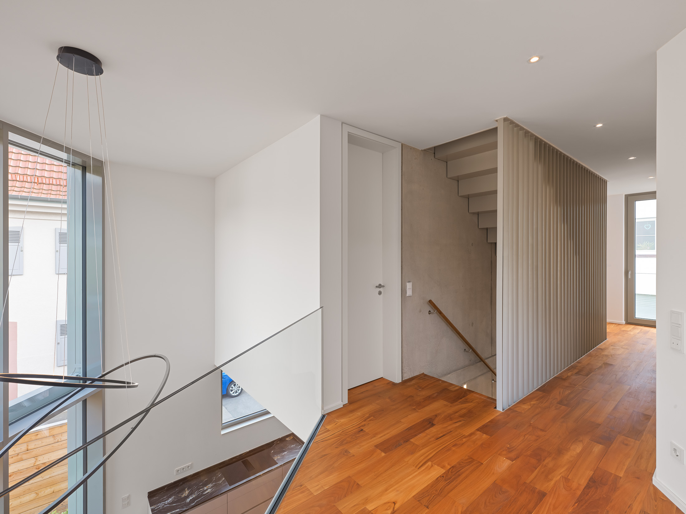 Zentraler Treppenaufgang entlang einer dreigeschossigen Sichtbetonwand als vertikales Erschließungselement im kompakten Einfamilienhaus.