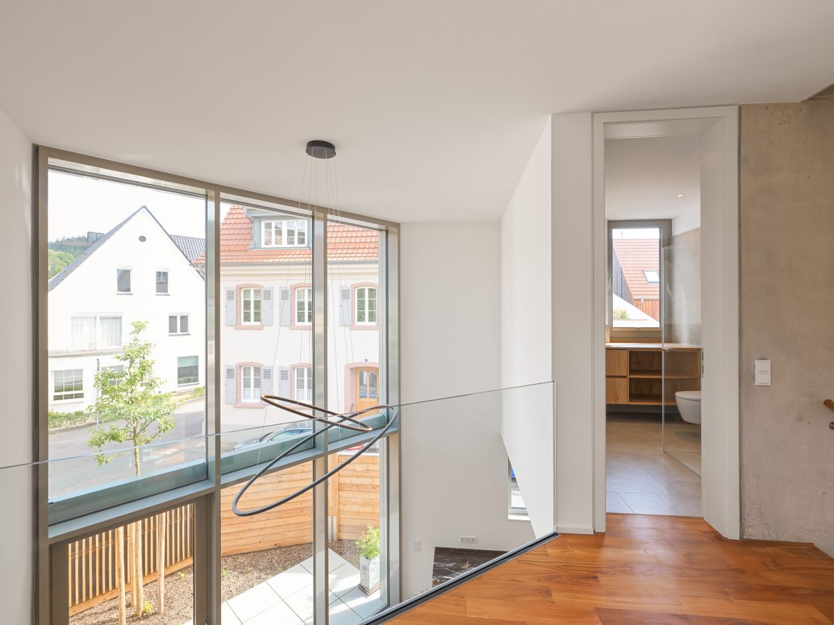 Mehrgeschossiger Luftraum über dem Wohnbereich mit Blick auf die zweigeschossige Pfosten-Riegel-Fassade und die bewaldete Hügellandschaft des Odenwaldes.