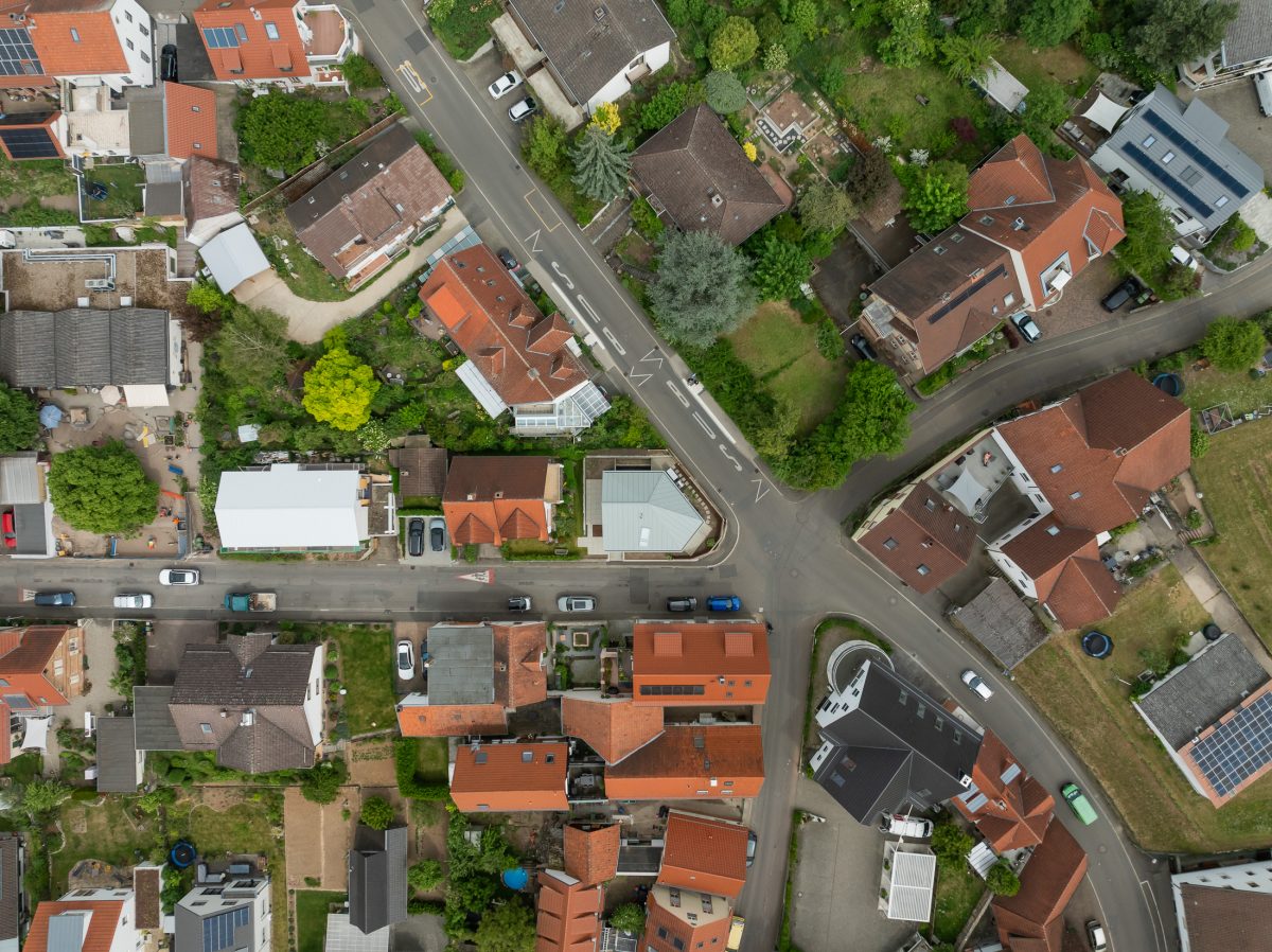 Monolithisches, kompaktes Wohnhaus mit polygonalem Grundriss und asymmetrischem Walmdach aus anthrazitfarbenem Stehfalzblech an einer markanten Verkehrskreuzung.