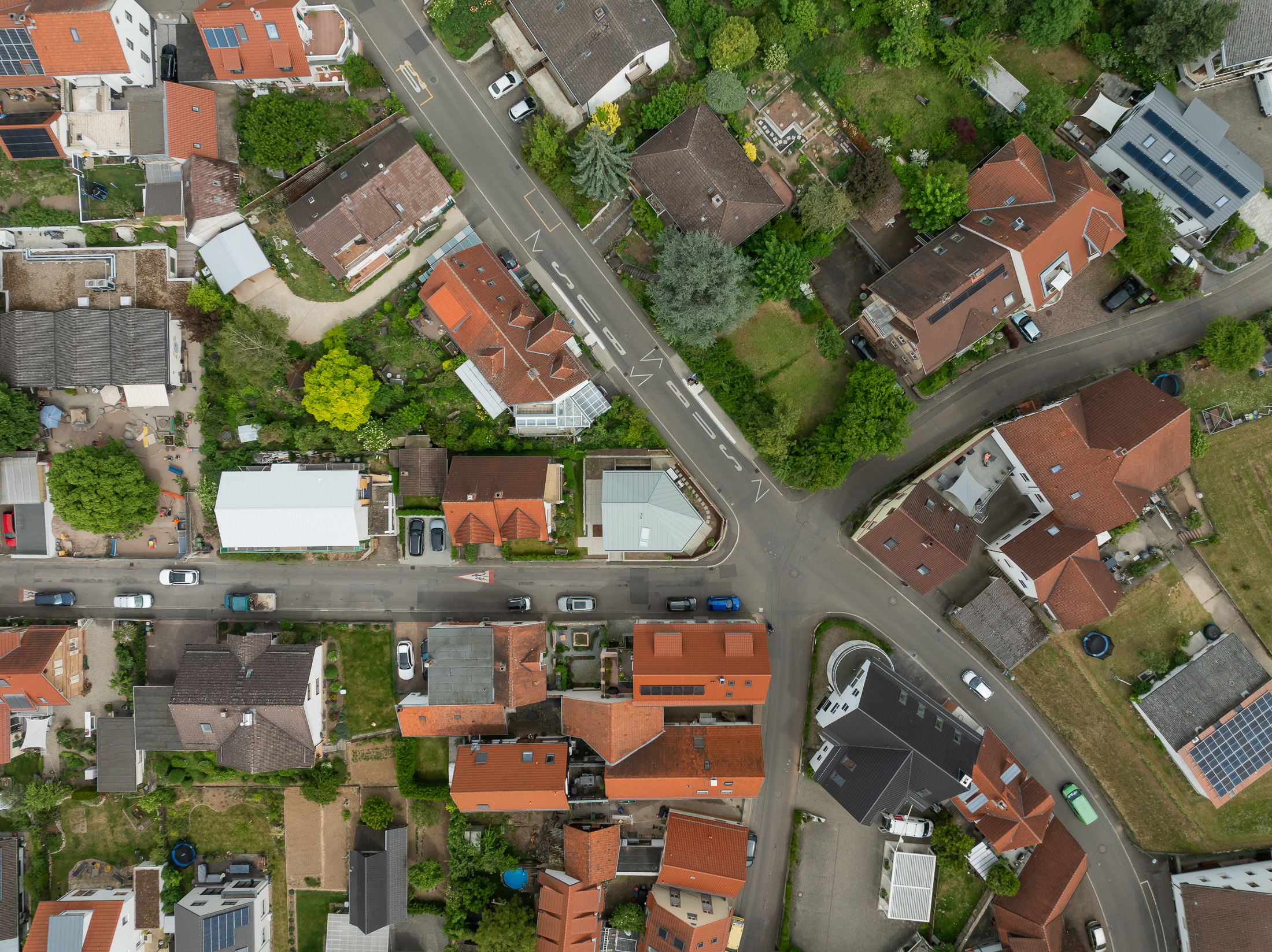 Monolithisches, kompaktes Wohnhaus mit polygonalem Grundriss und asymmetrischem Walmdach aus anthrazitfarbenem Stehfalzblech an einer markanten Verkehrskreuzung.