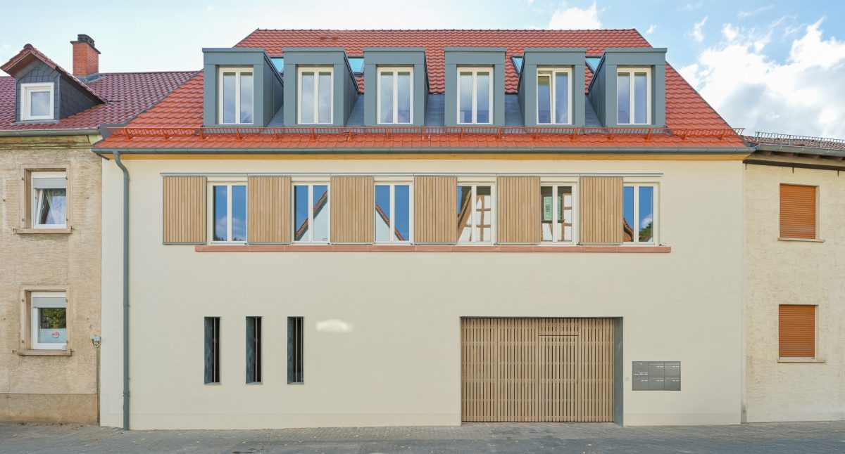 Neubau eines modernen Mehrfamilienhauses mit begrüntem Innenhof im historischen Kontext mit Besenstrichputz, Holzschalung, Schiebeläden und modernen Gauben.