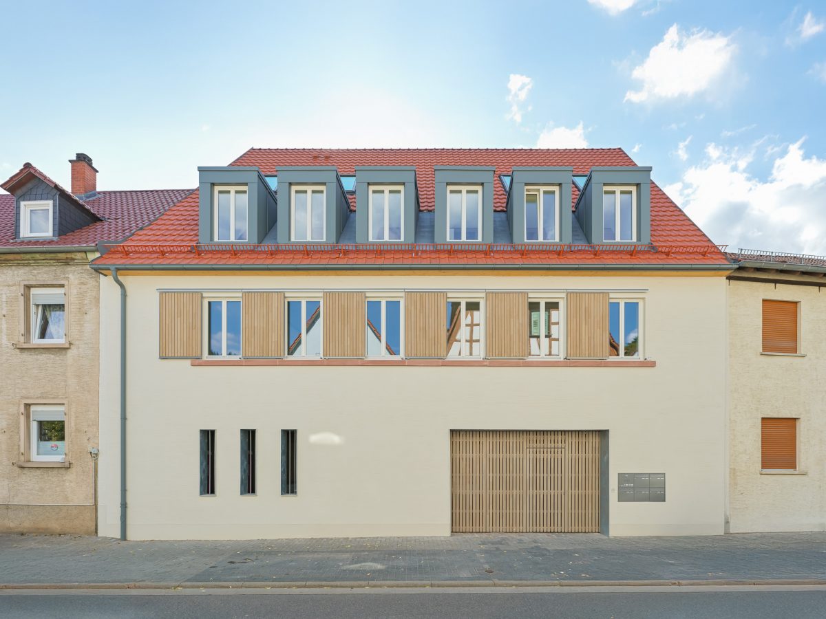 Neubau eines modernen Mehrfamilienhauses mit begrüntem Innenhof im historischen Kontext mit Besenstrichputz, Holzschalung, Schiebeläden und modernen Gauben.