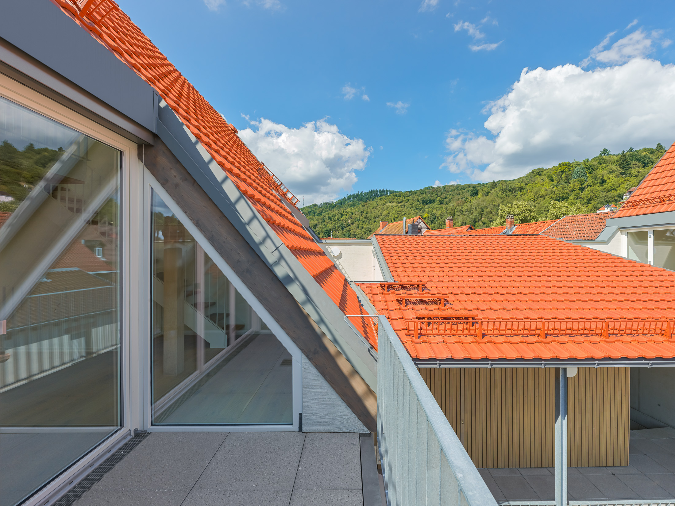 Neubau eines modernen Mehrfamilienhauses - Dachloggia mit Blick über die Dachlandschaft und bewaldeten Hügel