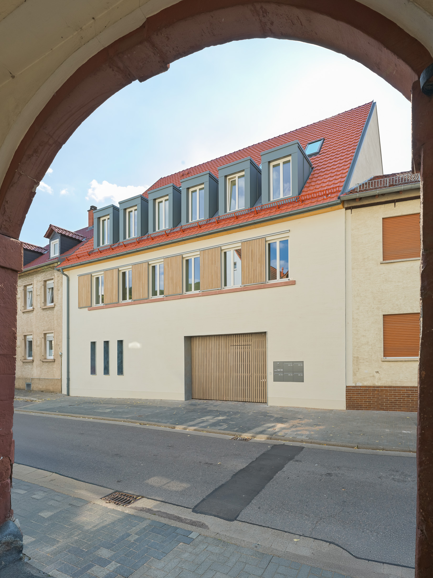 Neubau eines modernen Mehrfamilienhauses mit begrüntem Innenhof im historischen Kontext mit Besenstrichputz, Holzschalung, Schiebeläden und modernen Gauben.