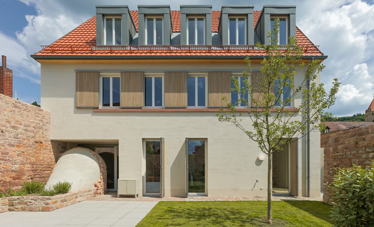 Neubau eines modernen Mehrfamilienhauses mit begrüntem Innenhof im historischen Kontext mit Besenstrichputz, Holzschalung, Schiebeläden und modernen Gauben. Grüner Hinterhof mit Zugang zum historischen Gewölbekeller.