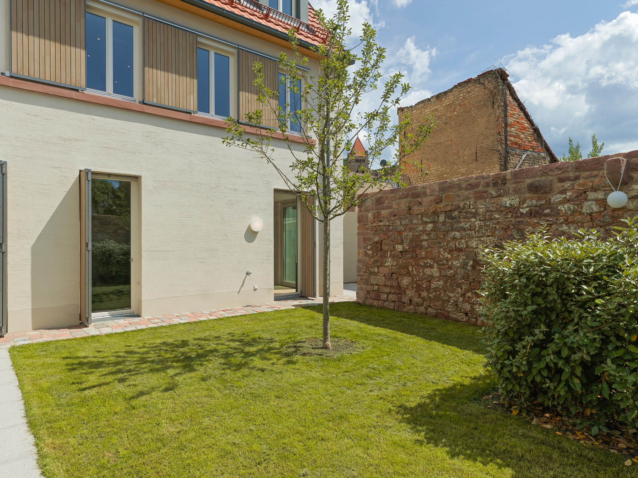 Neubau eines modernen Mehrfamilienhauses mit begrüntem Innenhof im historischen Kontext mit Besenstrichputz, Holzschalung, Schiebeläden und modernen Gauben.