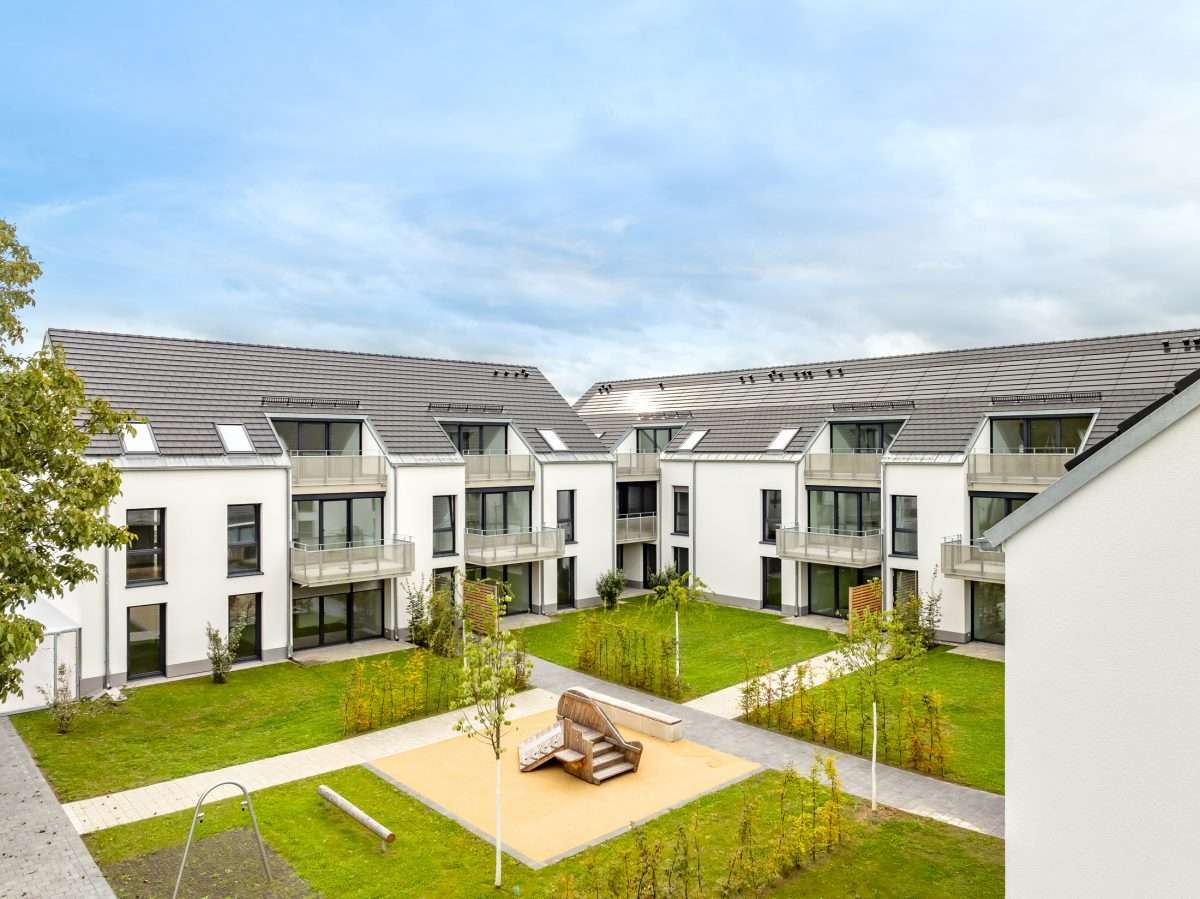 Mehrfamilienhausanlage für die VOLKSWOHNUNG GmbH in Karlsruhe-Durlach mit zweigeschossigen Hausgruppen und prägnanten Satteldächern, die sich um zwei begrünte, geschützte Innenhöfe organisieren; großzügige Verglasungen, Loggien und Dachgauben sowie eine flächenbündig integrierte Indach-Photovoltaikanlage prägen das architektonische Erscheinungsbild.