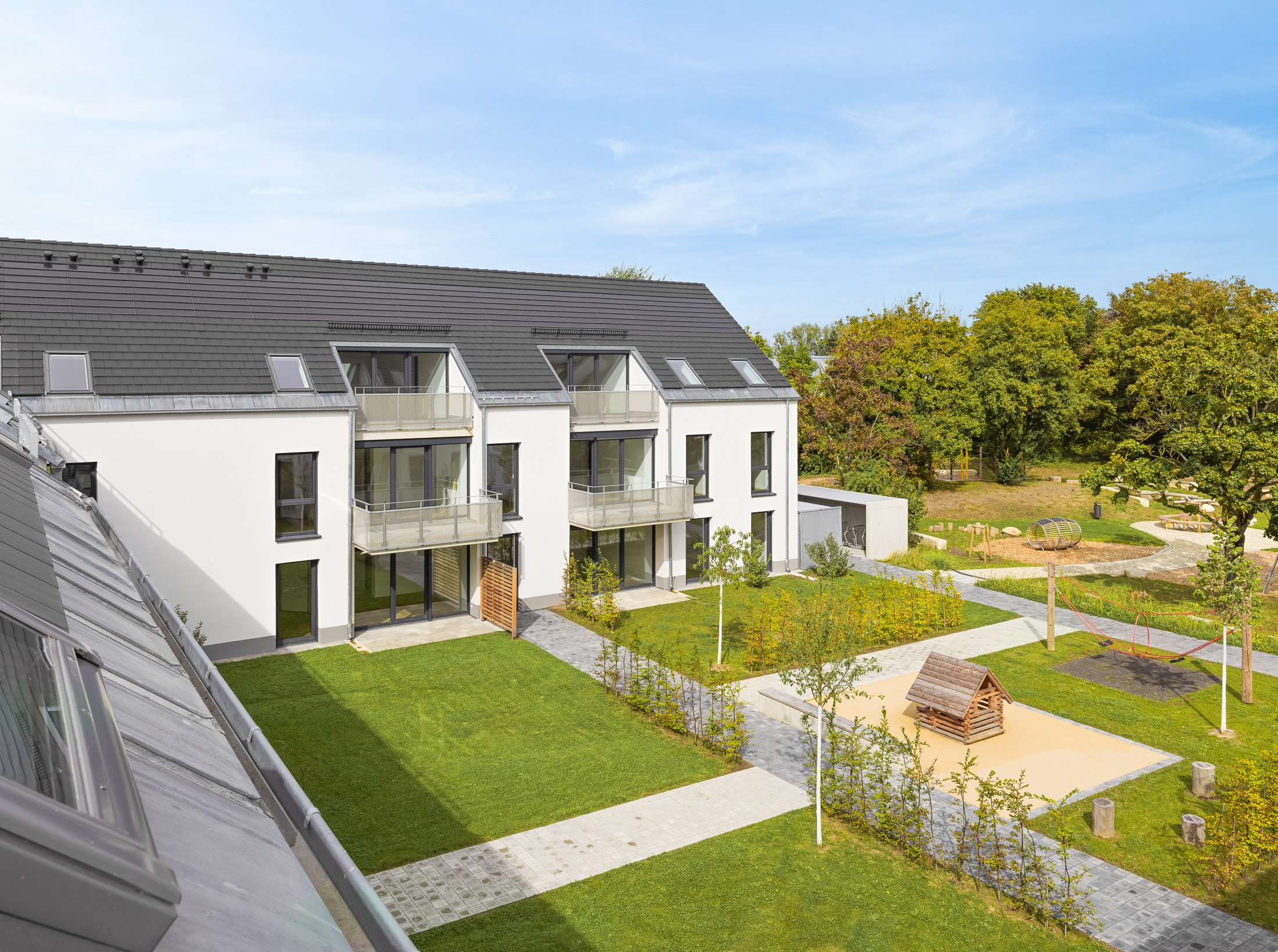 Mehrfamilienhausanlage für die VOLKSWOHNUNG GmbH in Karlsruhe-Durlach mit zweigeschossigen Hausgruppen und prägnanten Satteldächern, die sich um zwei begrünte, geschützte Innenhöfe organisieren; großzügige Verglasungen, Loggien und Dachgauben sowie eine flächenbündig integrierte Indach-Photovoltaikanlage prägen das architektonische Erscheinungsbild.