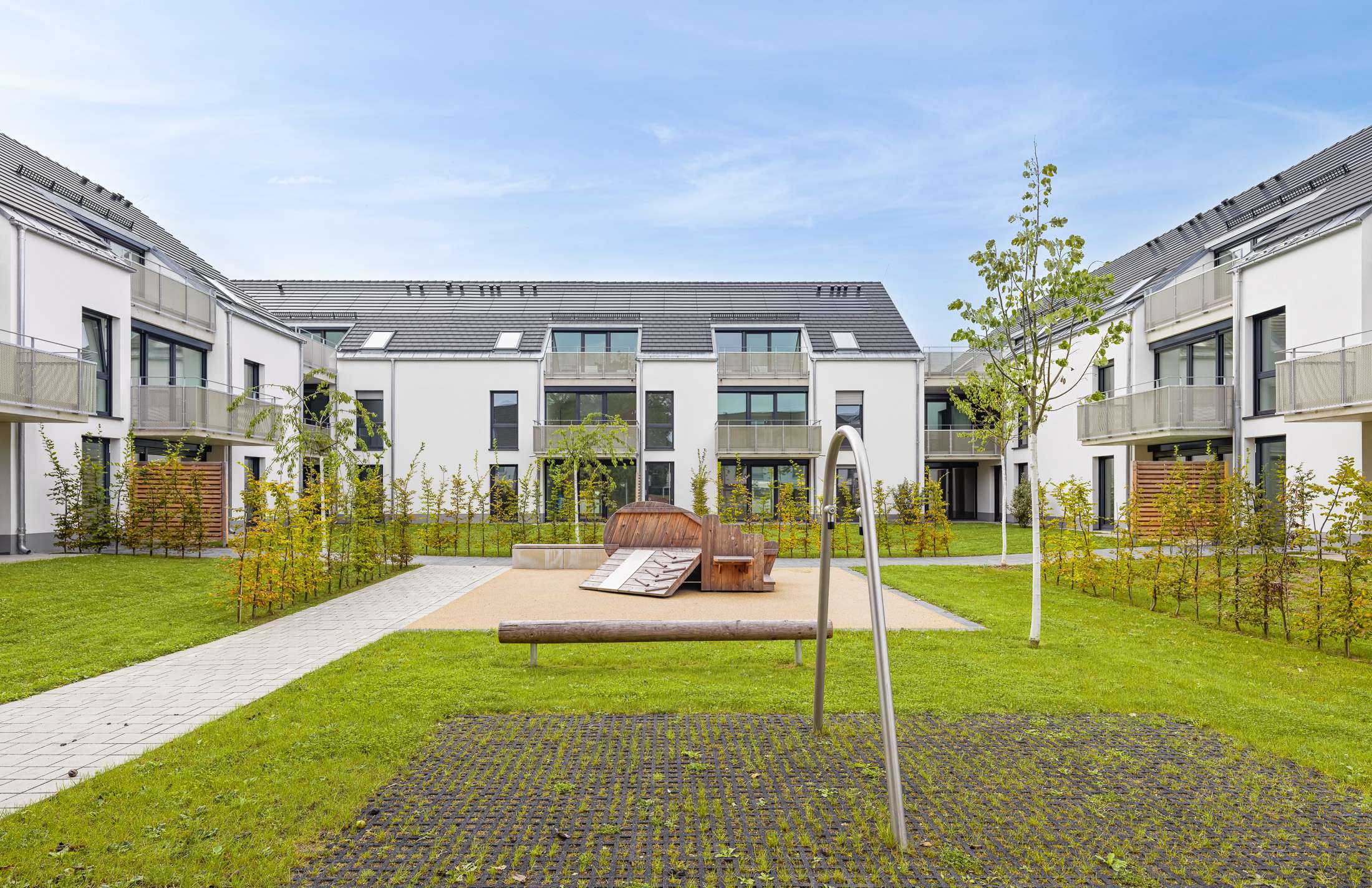 Mehrfamilienhausanlage für die VOLKSWOHNUNG GmbH in Karlsruhe-Durlach mit zweigeschossigen Hausgruppen und prägnanten Satteldächern, die sich um zwei begrünte, geschützte Innenhöfe organisieren; großzügige Verglasungen, Loggien und Dachgauben sowie eine flächenbündig integrierte Indach-Photovoltaikanlage prägen das architektonische Erscheinungsbild.