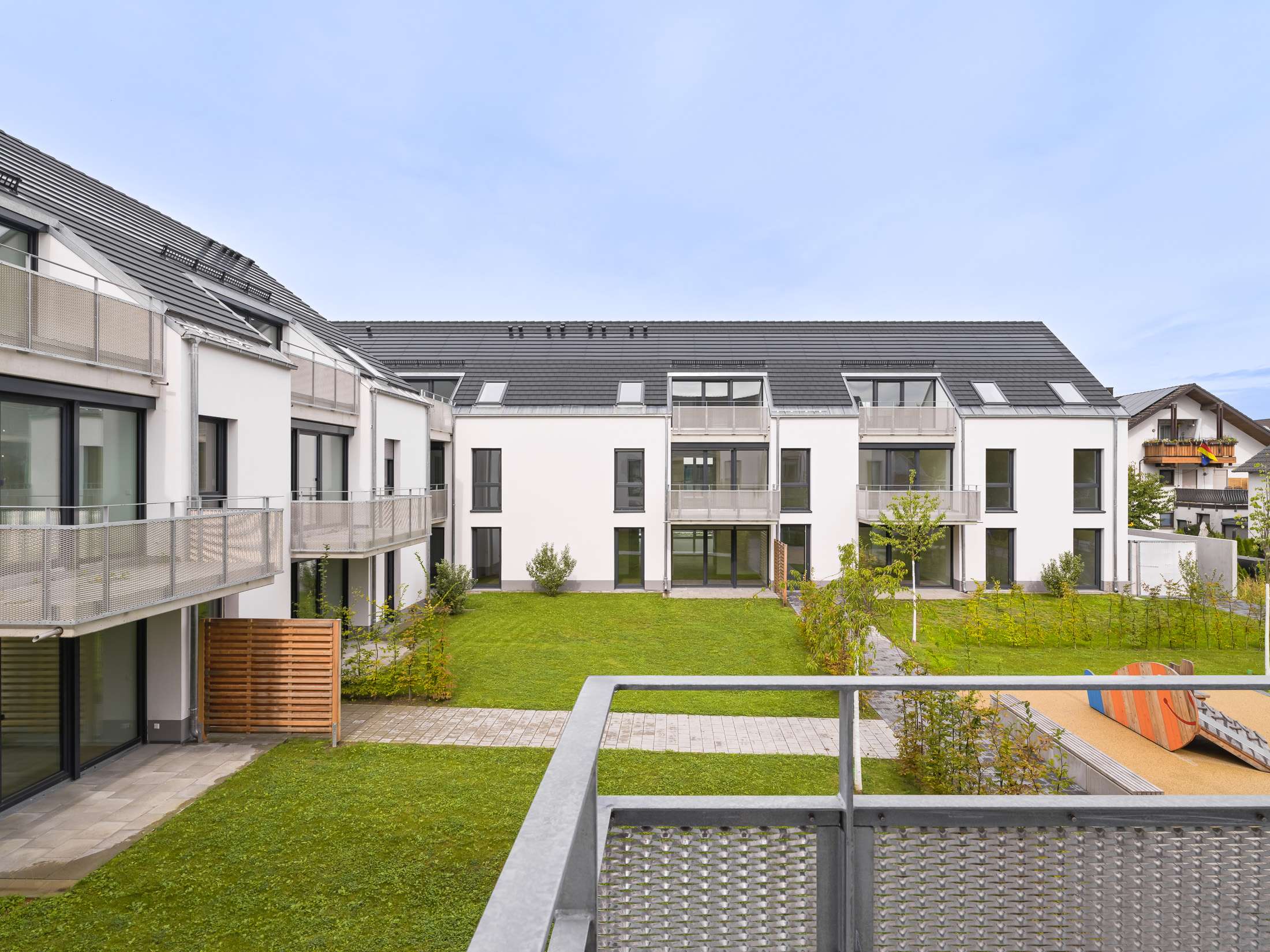 Mehrfamilienhausanlage für die VOLKSWOHNUNG GmbH in Karlsruhe-Durlach mit zweigeschossigen Hausgruppen und prägnanten Satteldächern, die sich um zwei begrünte, geschützte Innenhöfe organisieren; großzügige Verglasungen, Loggien und Dachgauben sowie eine flächenbündig integrierte Indach-Photovoltaikanlage prägen das architektonische Erscheinungsbild.