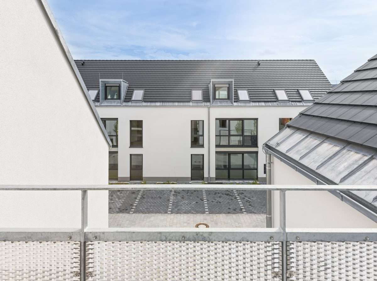 Mehrfamilienhausanlage für die VOLKSWOHNUNG GmbH in Karlsruhe-Durlach mit zweigeschossigen Hausgruppen und prägnanten Satteldächern, die sich um zwei begrünte, geschützte Innenhöfe organisieren; großzügige Verglasungen, Loggien und Dachgauben sowie eine flächenbündig integrierte Indach-Photovoltaikanlage prägen das architektonische Erscheinungsbild.