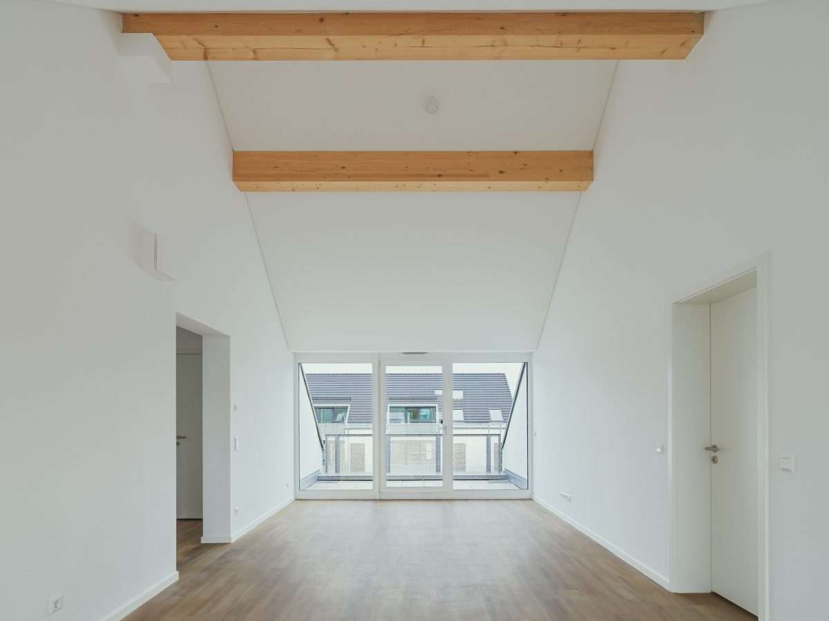 Mehrfamilienhausanlage für die VOLKSWOHNUNG GmbH in Karlsruhe-Durlach mit zweigeschossigen Hausgruppen und prägnanten Satteldächern, die sich um zwei begrünte, geschützte Innenhöfe organisieren; großzügige Verglasungen, Loggien und Dachgauben sowie eine flächenbündig integrierte Indach-Photovoltaikanlage prägen das architektonische Erscheinungsbild.