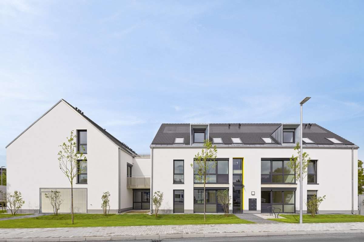 Mehrfamilienhausanlage für die VOLKSWOHNUNG GmbH in Karlsruhe-Durlach mit zweigeschossigen Hausgruppen und prägnanten Satteldächern, die sich um zwei begrünte, geschützte Innenhöfe organisieren; großzügige Verglasungen, Loggien und Dachgauben sowie eine flächenbündig integrierte Indach-Photovoltaikanlage prägen das architektonische Erscheinungsbild.