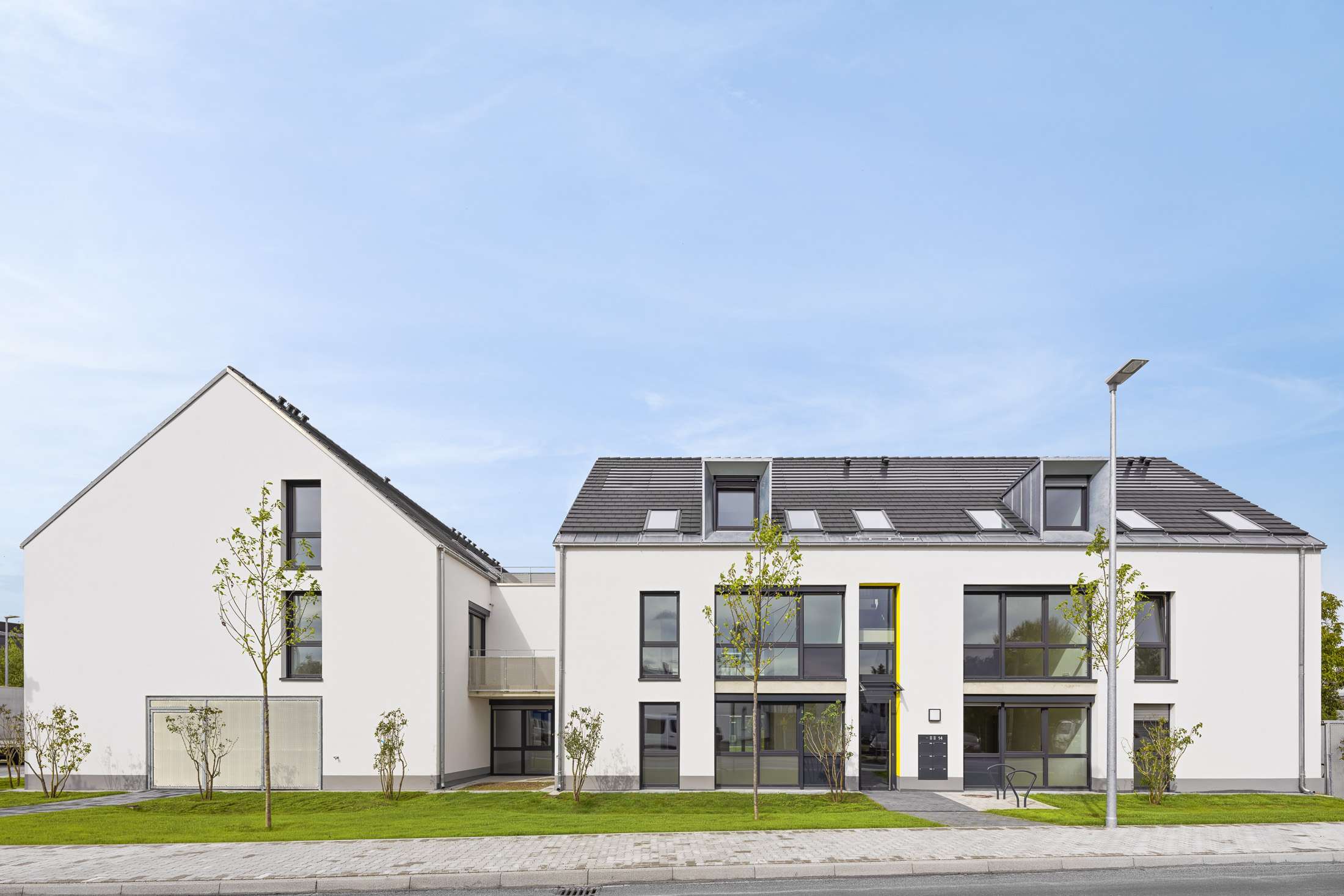 Mehrfamilienhausanlage für die VOLKSWOHNUNG GmbH in Karlsruhe-Durlach mit zweigeschossigen Hausgruppen und prägnanten Satteldächern, die sich um zwei begrünte, geschützte Innenhöfe organisieren; großzügige Verglasungen, Loggien und Dachgauben sowie eine flächenbündig integrierte Indach-Photovoltaikanlage prägen das architektonische Erscheinungsbild.