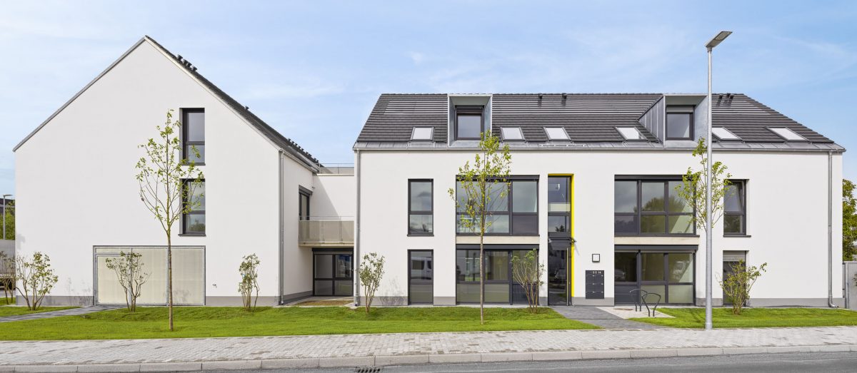 Mehrfamilienhausanlage für die VOLKSWOHNUNG GmbH in Karlsruhe-Durlach mit zweigeschossigen Hausgruppen und prägnanten Satteldächern, die sich um zwei begrünte, geschützte Innenhöfe organisieren; großzügige Verglasungen, Loggien und Dachgauben sowie eine flächenbündig integrierte Indach-Photovoltaikanlage prägen das architektonische Erscheinungsbild.
