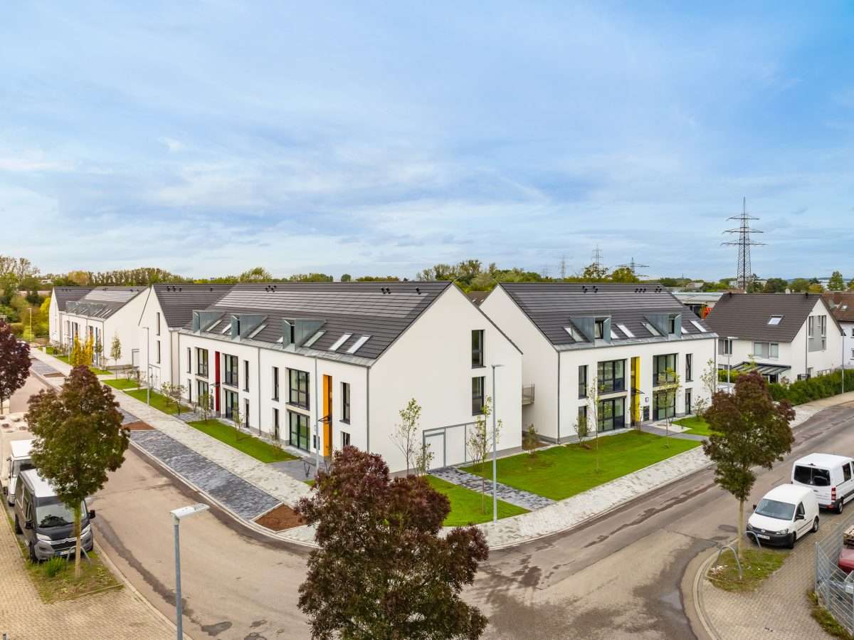 Mehrfamilienhausanlage für die VOLKSWOHNUNG GmbH in Karlsruhe-Durlach mit zweigeschossigen Hausgruppen und prägnanten Satteldächern, die sich um zwei begrünte, geschützte Innenhöfe organisieren; großzügige Verglasungen, Loggien und Dachgauben sowie eine flächenbündig integrierte Indach-Photovoltaikanlage prägen das architektonische Erscheinungsbild.