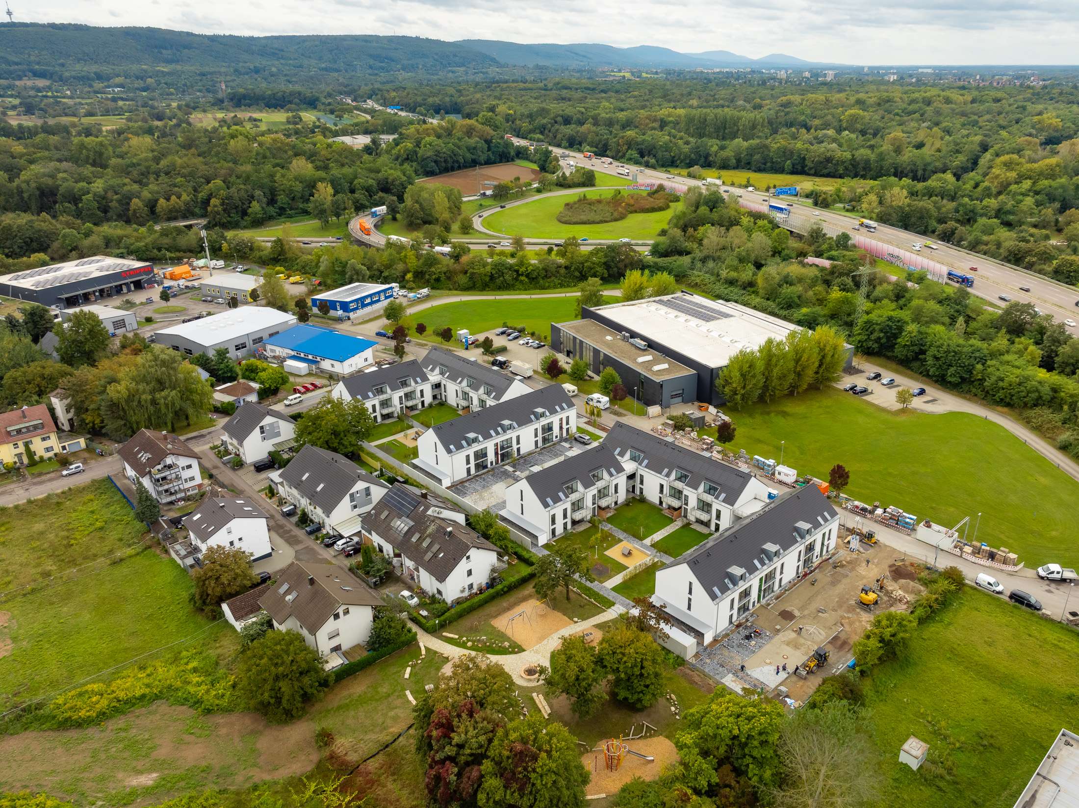 Mehrfamilienhausanlage für die VOLKSWOHNUNG GmbH in Karlsruhe-Durlach mit zweigeschossigen Hausgruppen und prägnanten Satteldächern, die sich um zwei begrünte, geschützte Innenhöfe organisieren; großzügige Verglasungen, Loggien und Dachgauben sowie eine flächenbündig integrierte Indach-Photovoltaikanlage prägen das architektonische Erscheinungsbild.