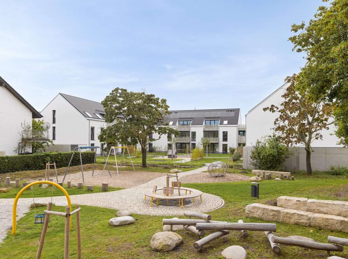 Mehrfamilienhausanlage für die VOLKSWOHNUNG GmbH in Karlsruhe-Durlach mit zweigeschossigen Hausgruppen und prägnanten Satteldächern, die sich um zwei begrünte, geschützte Innenhöfe organisieren; großzügige Verglasungen, Loggien und Dachgauben sowie eine flächenbündig integrierte Indach-Photovoltaikanlage prägen das architektonische Erscheinungsbild.