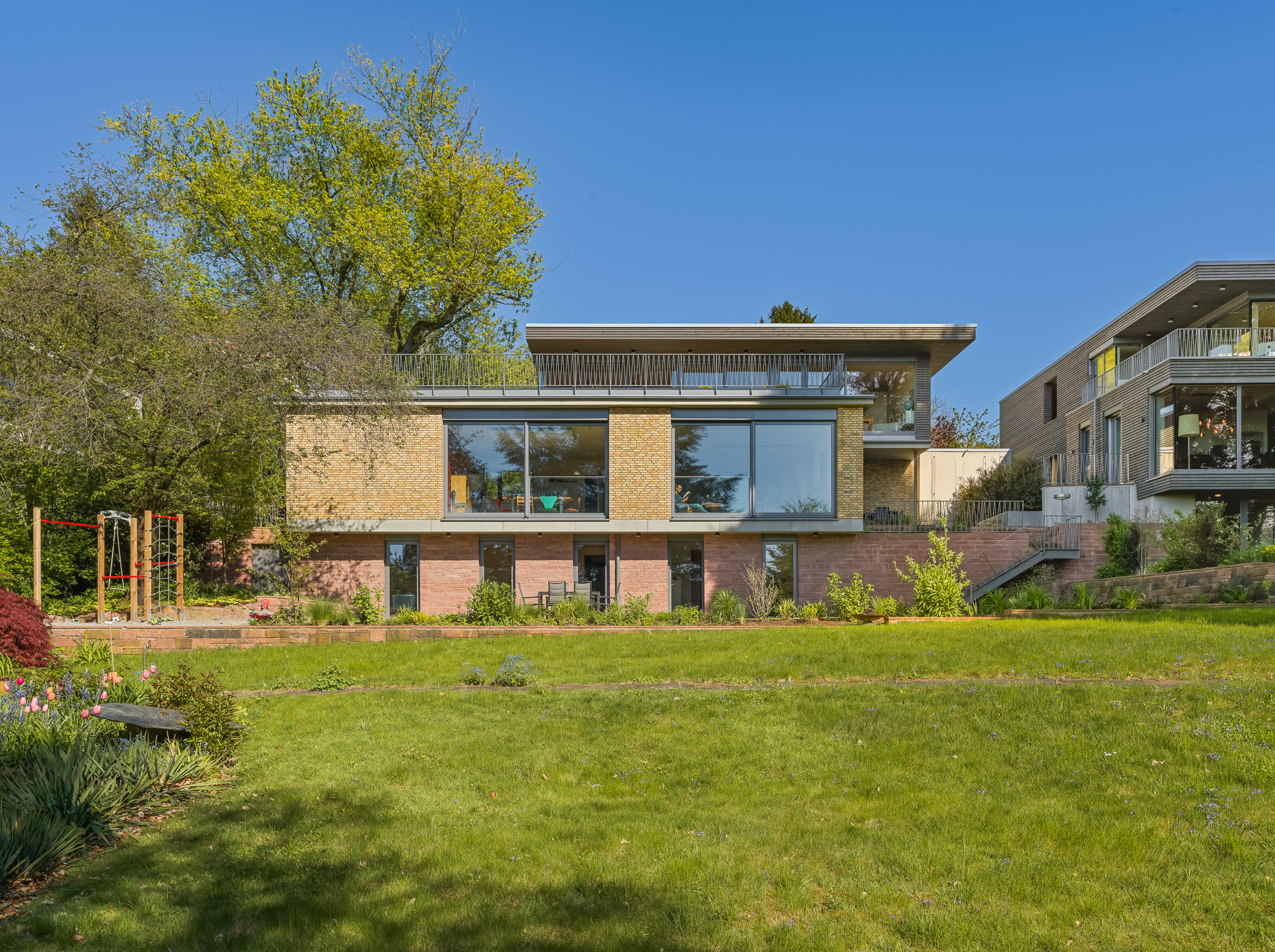 Architekturprojekt „Weiterbauen“ in Weinheim von Weber und Partner Architekten: Gesamtansicht der nachverdichteten Unternehmervilla aus den 1950er Jahren im parkartigen Hanggrundstück. Der gekürzte Bestandsbau mit hellen Klinkern und Holzaufstockung verbindet sich durch den Sandsteinsockel mit dem modernen Erweiterungsbau aus Massivholz.