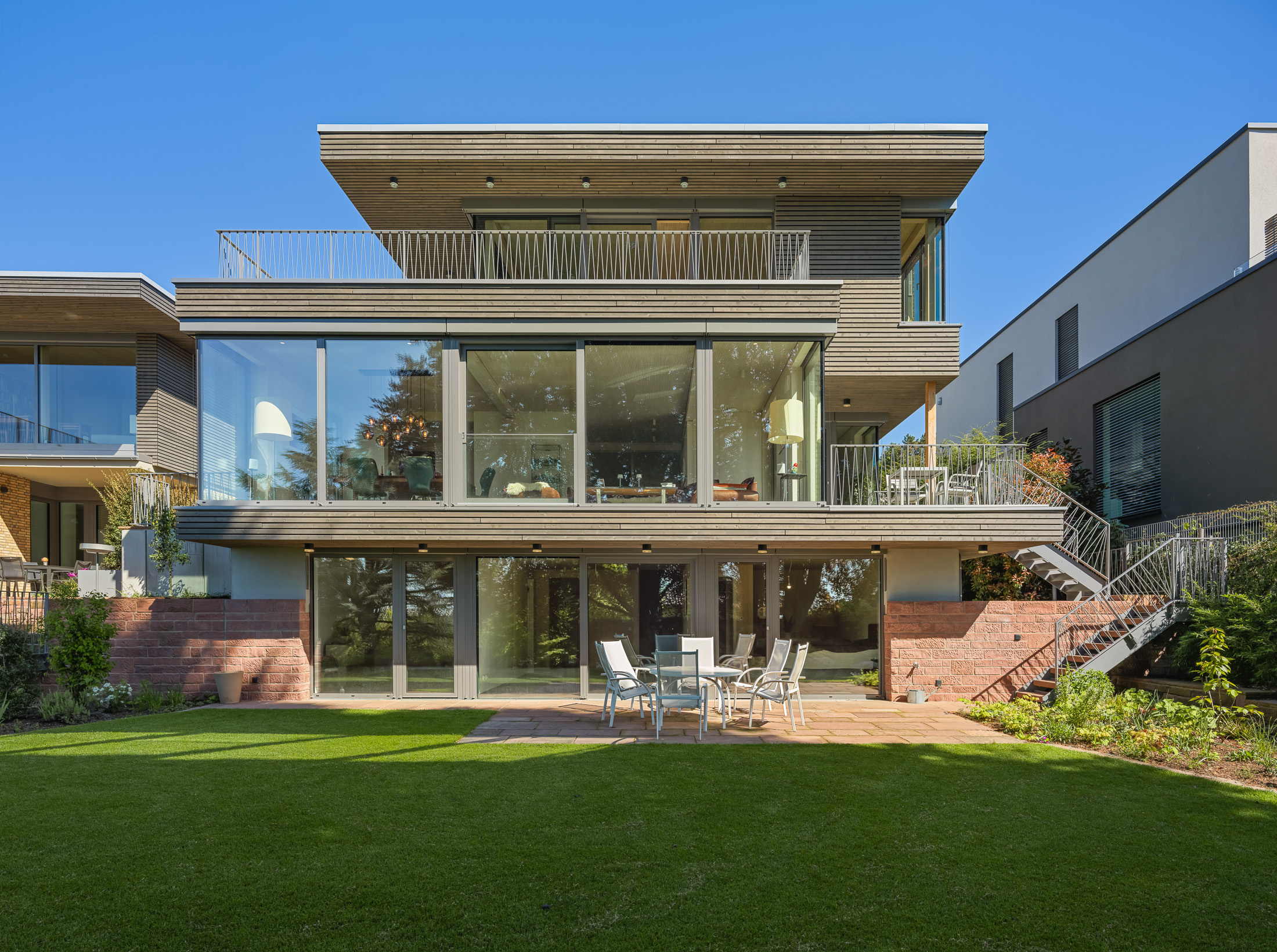 Architekturprojekt „Weiterbauen“ in Weinheim von Weber und Partner Architekten: Gesamtansicht der nachverdichteten Unternehmervilla aus den 1950er Jahren im parkartigen Hanggrundstück. Der gekürzte Bestandsbau mit hellen Klinkern und Holzaufstockung verbindet sich durch den Sandsteinsockel mit dem modernen Erweiterungsbau aus Massivholz.