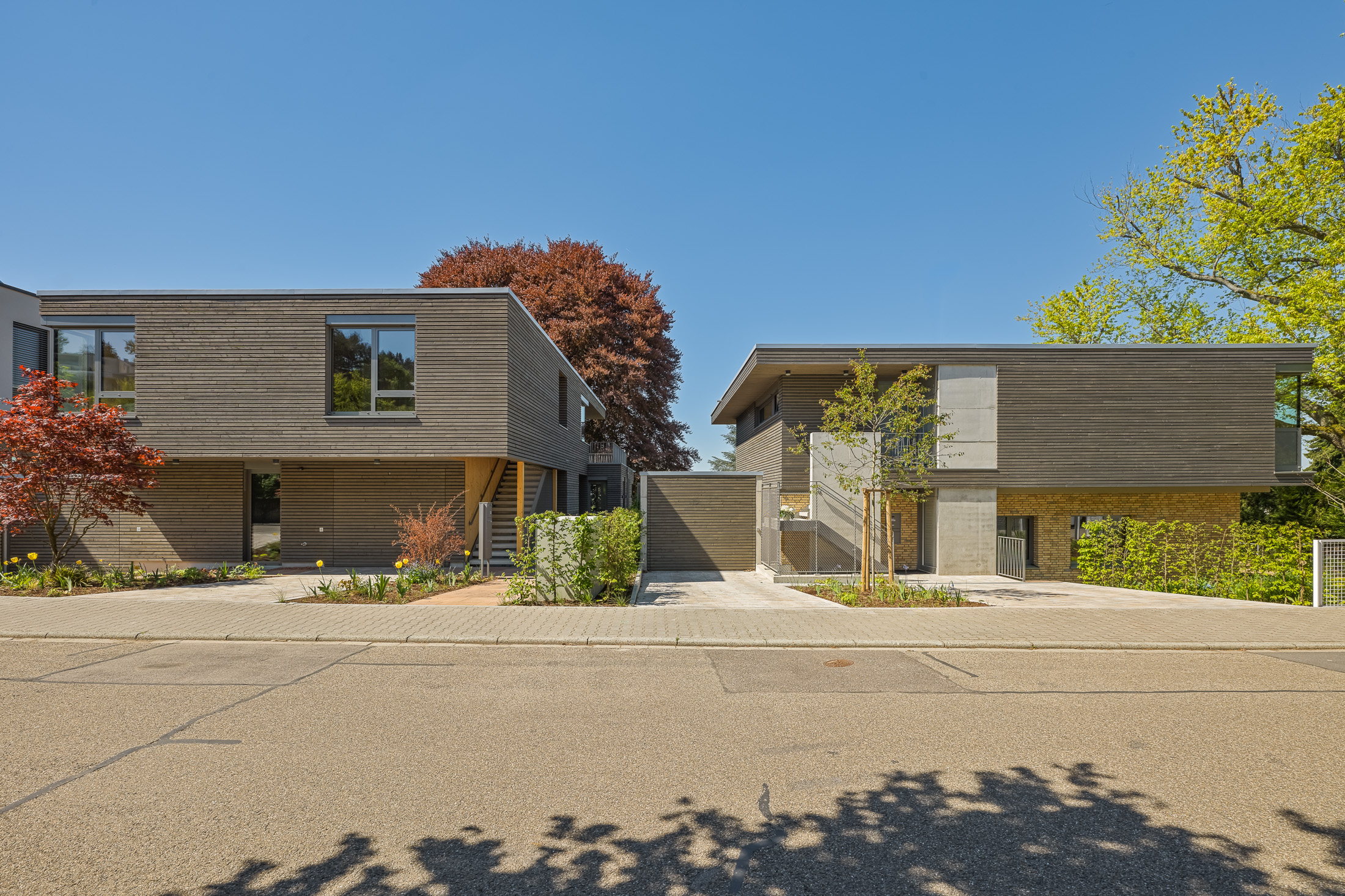 Architekturprojekt „Weiterbauen“ in Weinheim von Weber und Partner Architekten: Gesamtansicht der nachverdichteten Unternehmervilla aus den 1950er Jahren im parkartigen Hanggrundstück. Der gekürzte Bestandsbau mit hellen Klinkern und Holzaufstockung verbindet sich durch den Sandsteinsockel mit dem modernen Erweiterungsbau aus Massivholz.