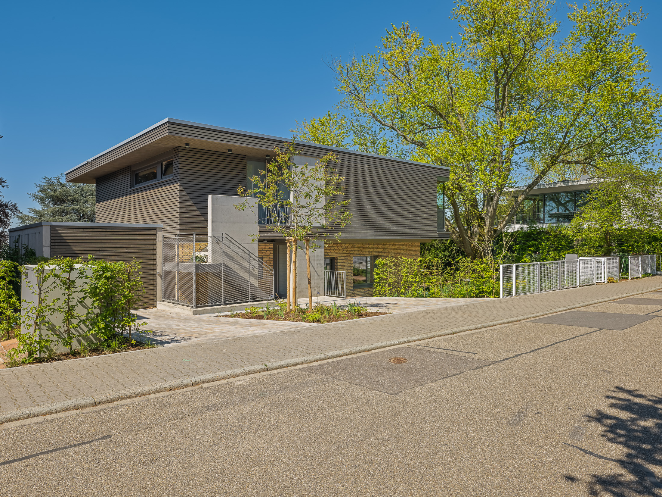 Architekturprojekt „Weiterbauen“ in Weinheim von Weber und Partner Architekten: Gesamtansicht der nachverdichteten Unternehmervilla aus den 1950er Jahren im parkartigen Hanggrundstück. Der gekürzte Bestandsbau mit hellen Klinkern und Holzaufstockung verbindet sich durch den Sandsteinsockel mit dem modernen Erweiterungsbau aus Massivholz.