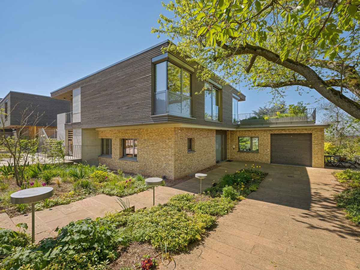 Architekturprojekt „Weiterbauen“ in Weinheim von Weber und Partner Architekten: Gesamtansicht der nachverdichteten Unternehmervilla aus den 1950er Jahren im parkartigen Hanggrundstück. Der gekürzte Bestandsbau mit hellen Klinkern und Holzaufstockung verbindet sich durch den Sandsteinsockel mit dem modernen Erweiterungsbau aus Massivholz.
