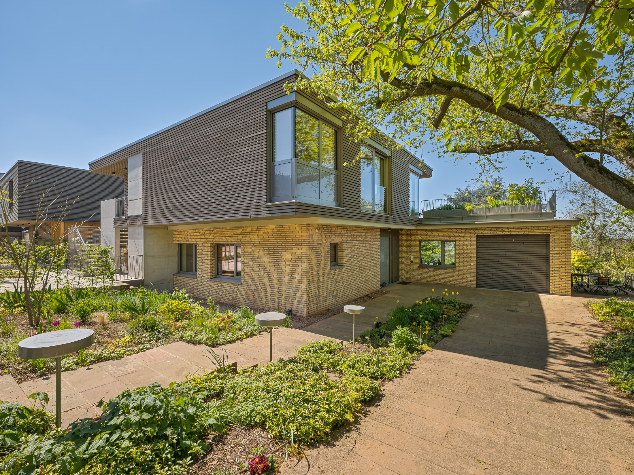 Architekturprojekt „Weiterbauen“ in Weinheim von Weber und Partner Architekten: Gesamtansicht der nachverdichteten Unternehmervilla aus den 1950er Jahren im parkartigen Hanggrundstück. Der gekürzte Bestandsbau mit hellen Klinkern und Holzaufstockung verbindet sich durch den Sandsteinsockel mit dem modernen Erweiterungsbau aus Massivholz.